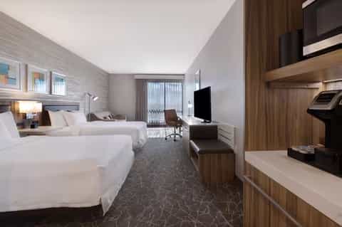 Modern hotel guest room with two queen beds, work desk, flat-screen TV, and contemporary wood furnishings
