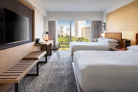 Hotel guest room with two queen beds, city views, desk area, and modern wood furnishings