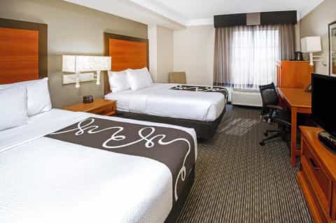 Modern hotel room with two queen beds, orange headboards, desk area, and contemporary furnishings