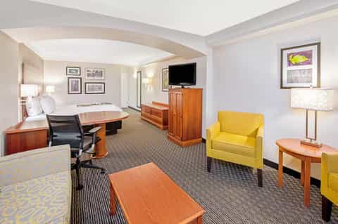 Spacious hotel suite with king bed, yellow accent chair, wood furniture, and curved ceiling details