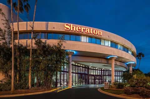 Curved Sheraton hotel entrance with terracotta brick facade, glass doors, and palm trees at dusk