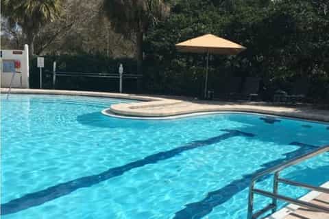 Olympic-style lap pool with lane dividers, lounge chairs, and tan umbrella in sunny outdoor setting