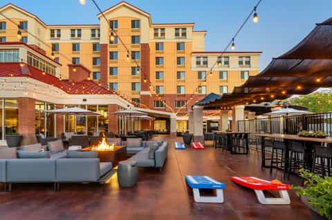 Resort courtyard at dusk with fireplace, lounge seating, cornhole games, and brick hotel building