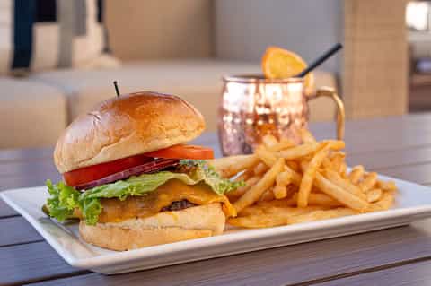 Gourmet burger with cheese and tomato served with fries and a citrus cocktail on a white plate