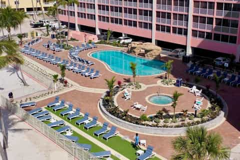 Aerial view of curved resort pool with lounge chairs, hot tub, and palm trees