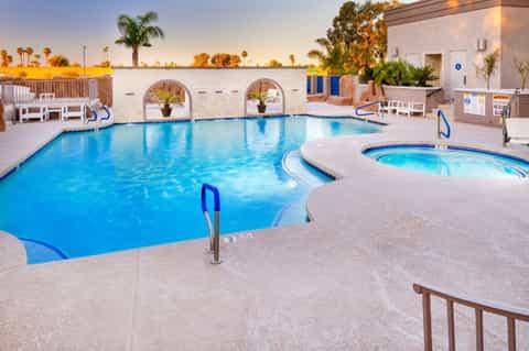 Resort swimming pool at dusk with spa tub, palm trees, and desert landscape