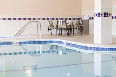 Indoor pool with blue tile border, lounge chairs, and modern seating area