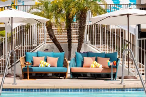 Beachside lounge seating with turquoise and coral cushions under white umbrellas and palm trees