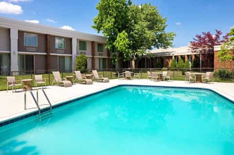 Outdoor swimming pool with lounge chairs and green landscaping beside brick hotel building