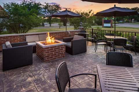 Outdoor patio with fire pit, lounge seating, umbrellas, and brick wall at dusk