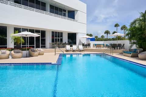 Modern resort pool with white umbrellas, lounge chairs and palm trees