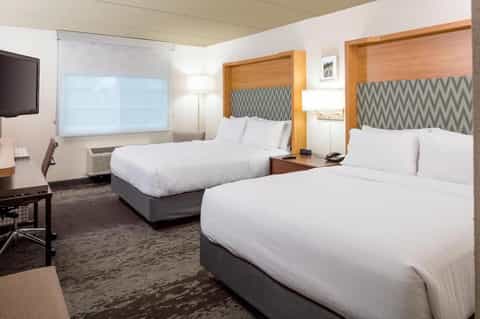 Hotel room with two queen beds, gray patterned headboards, and flat-screen television