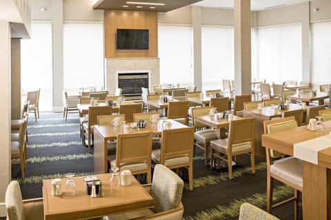Spacious dining room with wooden tables, chairs, fireplace, and abundant natural light from windows