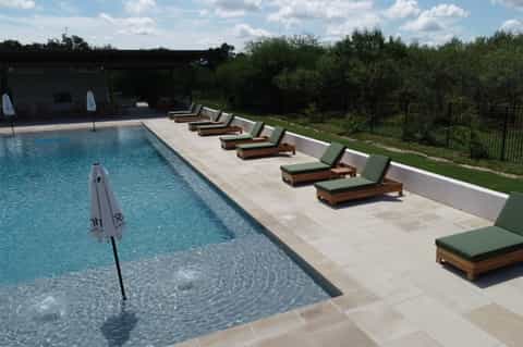 Resort lap pool with lounge chairs featuring green cushions, white umbrellas, and manicured lawn beyond