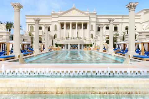 Luxurious neoclassical pool with grand columned building, blue loungers, and tropical setting