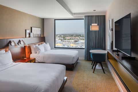 Modern hotel room with two queen beds, city skyline view through floor-to-ceiling window