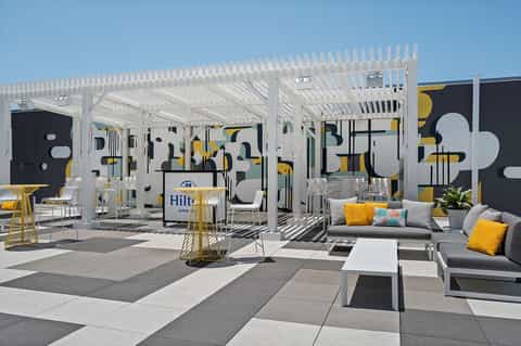 Contemporary poolside lounge with white pergola, yellow and gray seating, and abstract wall art