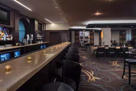 Upscale hotel bar and lounge with long counter, dark wood accents, and modern lighting