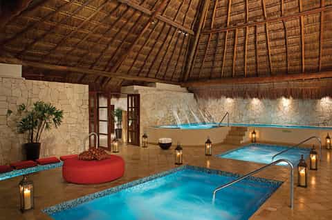 Spa hot tub area with thatched roof, stone walls, turquoise pools, and ambient candle lighting