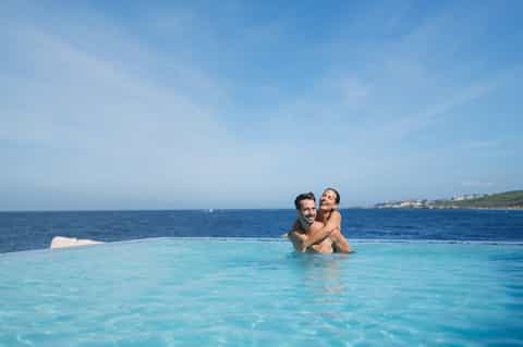 Couple enjoying infinity pool overlooking turquoise ocean and coastal landscape