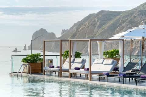 Oceanside pool cabanas with white curtains and loungers overlooking dramatic coastal cliffs