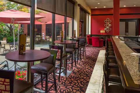 Modern hotel lounge with red accent walls, burgundy seating, patterned carpet, and outdoor patio view