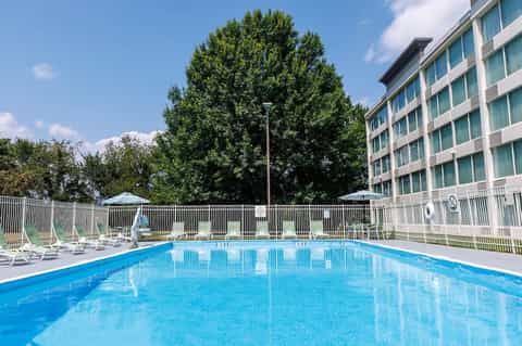 Resort outdoor swimming pool with lounge chairs, white railings, and multi-story hotel building