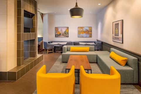 Modern hotel lounge with yellow accent chairs, gray seating, and fireplace