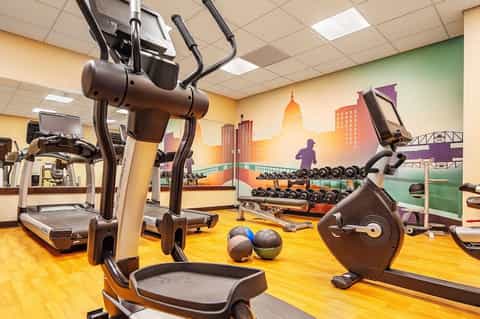 Modern gym interior with cardboard exercise bikes, weights, and city skyline mural