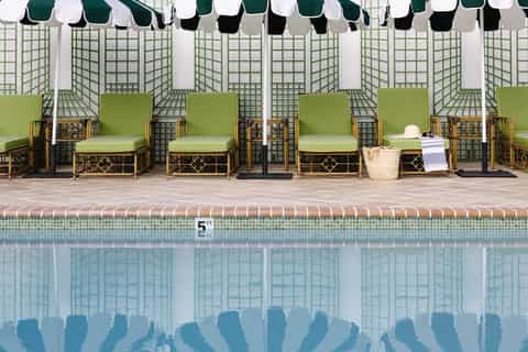 Resort pool with green lounge chairs under striped umbrellas and lattice privacy screens