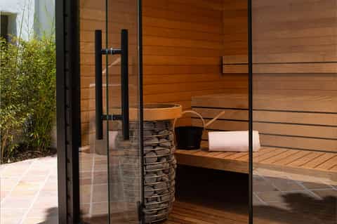 Modern spa sauna interior with wooden walls, glass door, stone heater, and rolled towels