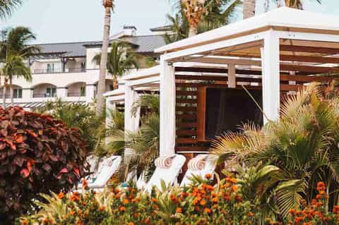 Tropical resort courtyard with white pergola, lounge chairs, flowering plants, and ocean-view building