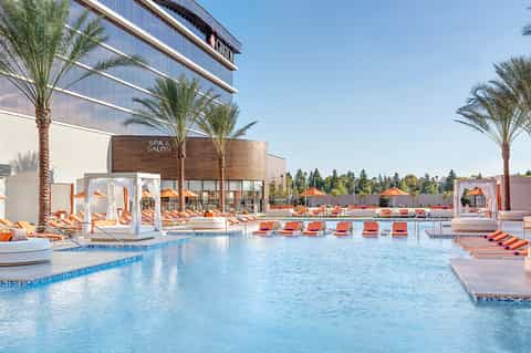 Modern spa and pool complex with orange loungers, contemporary architecture, palm trees, and mountain views
