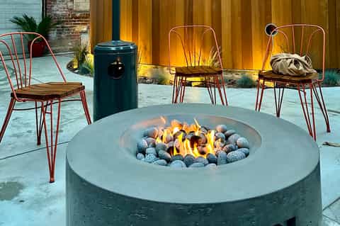 Outdoor fire pit seating area with metal chairs and wooden accent wall at night