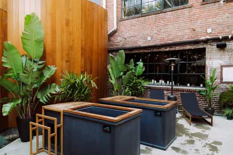 Outdoor courtyard with wooden hot tubs, tropical plants, brick building backdrop, and lounge chairs