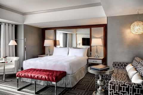 Luxurious hotel bedroom with white bedding, mirrored headboard, red bench, and contemporary furnishings