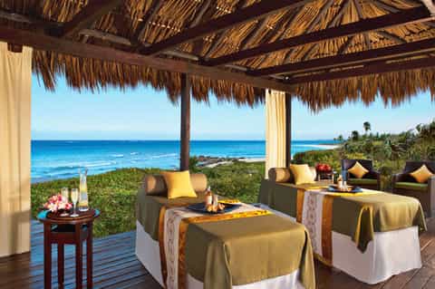 Beachfront spa pavilion with thatched roof, ocean views, and luxury lounging areas