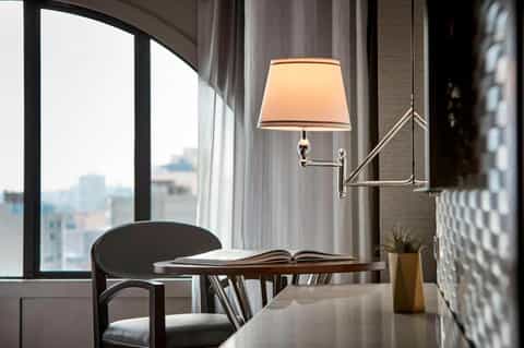 Elegant hotel room workspace with desk, modern lamp, and city skyline view through large window