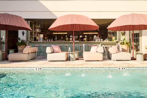 Resort poolside lounge with curved cream seating, red umbrellas, tiled bar, and crystal-clear water
