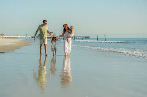 Family wading in shallow ocean water with pier visible in background
