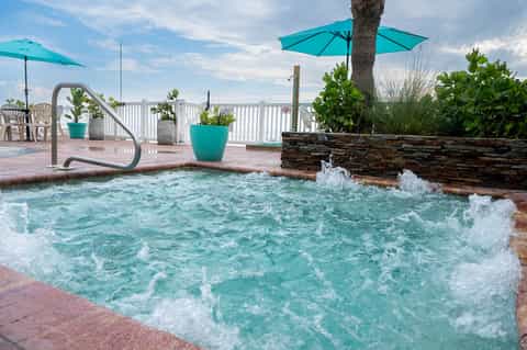 Spa hot tub with turquoise water and jets on rooftop terrace with white railing and teal umbrellas