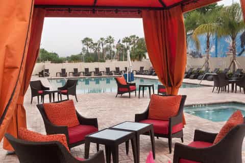 Resort pool area with red cabana drapes, lounge chairs, and palm trees in background