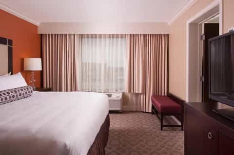 Hotel bedroom with queen bed, orange accent wall, beige curtains, and modern furnishings