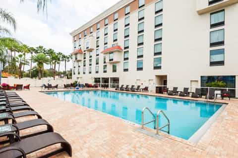 Resort pool with lounge chairs, palm trees, and multi-story hotel building in afternoon sunlight