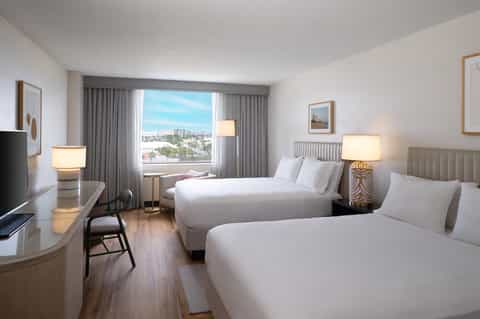Modern hotel room with two queen beds, city view, desk, and contemporary furnishings