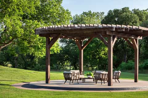 Wooden pergola structure with seating area in manicured green lawn