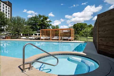 Resort pool with hot tub, lounge chairs, and modern wooden cabana structures under clear sky