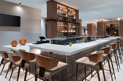 Contemporary bar with white counter, wooden chairs, and backlit liquor shelving