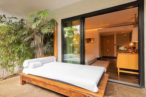 Modern bedroom with wooden bed, white bedding, and sliding glass doors opening to a patio garden