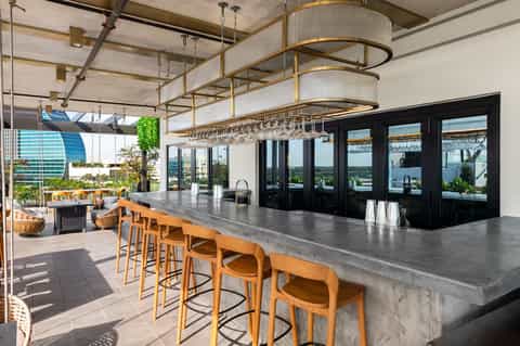 Modern rooftop bar with concrete countertop, wooden stools, pendant lighting, and panoramic waterfront views